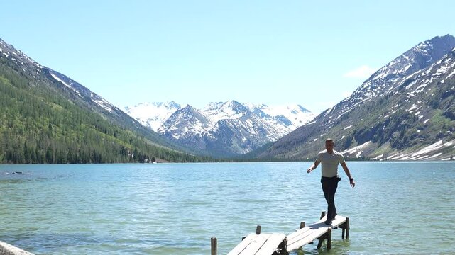 Man traveler in the mountains. Hiking in the Altai Mountains, a man poses against the backdrop of the Multinsky lakes, snowy mountain peaks in the distance in the background.