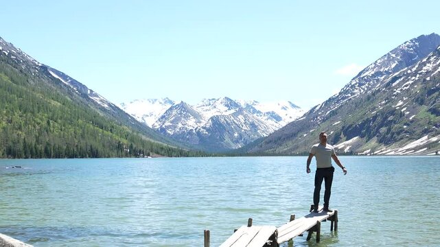 Man traveler in the mountains. Hiking in the Altai Mountains, a man poses against the backdrop of the Multinsky lakes, snowy mountain peaks in the distance in the background.