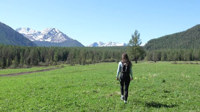 Backpacking in the mountains. A woman walks towards snowy peaks during a mountain hike.