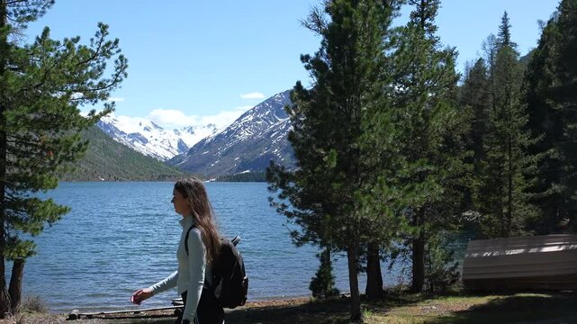 Traveling in the mountains. A woman travels in the mountains with a backpack, a woman walks along a mountain lake, snowy mountain peaks in the distance.