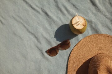 Overhead view of a beach towel with sunglasses and coconut drink under the sun at a tropical location