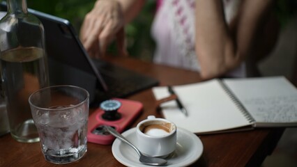 A mature woman sits at a cafe table, savoring her coffee while working on her laptop. She enjoys a productive day in a cozy atmosphere during her travels.