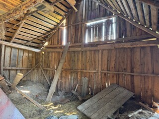 Fototapeta premium Interior of an old wooden shed with angled roof and scattered planks. Evokes rural life and rustic charm
