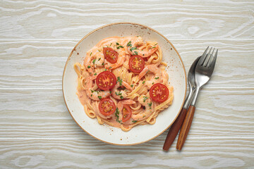 Seafood linguine pasta in creamy sauce with shrimp and cherry tomatoes, garnished with fresh parsley, served on white wooden background with cutlery top view