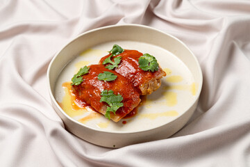 Two enchiladas draped in rich red sauce rest atop an elegant fabric, garnished with fresh cilantro, inviting culinary delight and flavor exploration