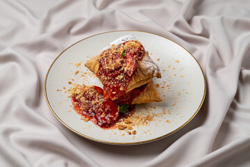 Flaky golden pastries rest elegantly on an ornate plate, drizzled with vibrant berry sauce and sprinkled with nut crumbs, inviting a sweet indulgence