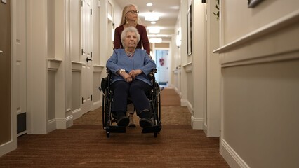 A caregiver guides an elderly woman in a wheelchair through a well-lit corridor of a nursing home, highlighting their bond and daily activities.