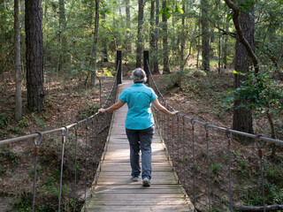 Senior Woman Walking on a Wooden Suspension Bridge in the Forest