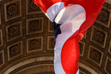 A large french flag is fluttering in the wind under the vault of the Triomphal Arch in Paris, France.