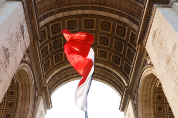 A large french flag is fluttering in the wind under the vault of the Triomphal Arch in Paris, France.