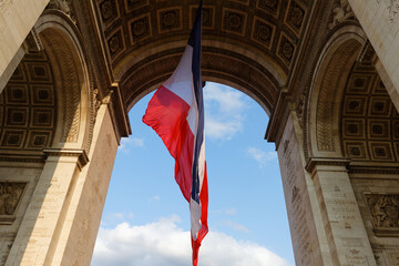 A large french flag is fluttering in the wind under the vault of the Triomphal Arch in Paris, France.