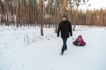 Dad with his daughter walking with snow tubing in the winter forest