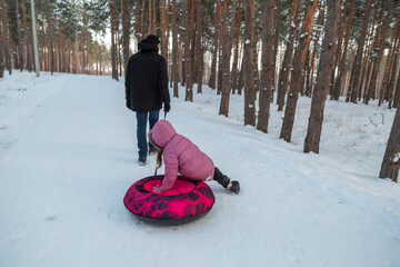 Dad with his daughter walking with snow tubing in the winter forest