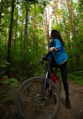 Fototapeta premium Beauty smiling woman biking on bicycle on spring trees green forest background, looking back. Enjoying fun girl outdoors. Female cyclist riding in park in sport fashion clothes. Full lenght