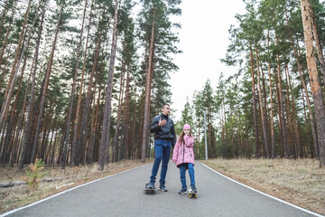 Obraz premium Father and his little daughter ride skateboards in the forest