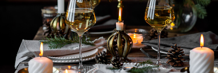 Banner. Beautiful table setting for family Christmas dinner at home. Cozy atmosphere, candlelight. Wine glasses, vintage chandelier, elegant interior. Fir tree branches, wooden furniture, dark, bokeh