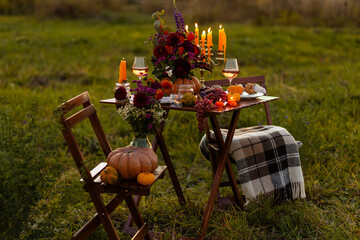 Elegant autumn decoration. Private wedding party for two, table set with floral decor, pumpkins, wine in field or meadow. Fall vibes, sunset, golden hour. Romantic surprise, marriage proposal