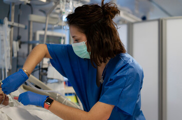 Nurse wearing surgical mask and gloves providing care to patient in hospital room