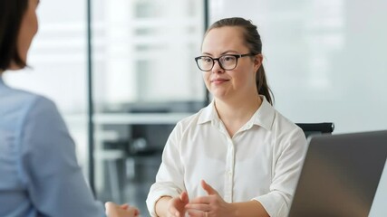 Smiling woman with down syndrome wearing white shirt shaking hands in modern office environment. Happy female employee greeting colleague professionally. Inclusion diversity concept for workplace