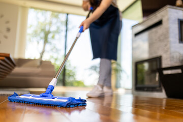 Person cleaning wooden floor with mop in bright modern living room during daytime