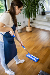 Woman cleaning wooden floor with mop in modern living room during daytime