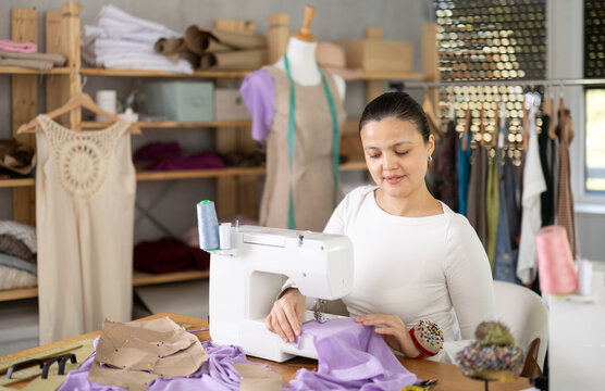 Glad young woman tailor making dress using stitching machine in sewing studio