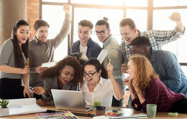Young designers team enjoying success, looking at computer screen, celebrating successful project, dealing contract, winning tender, copy space