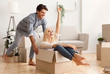 Moving New Apartment. Husband Having Fun Riding His Wife In Carton Box During Relocation