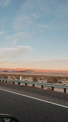Scenic Desert Road Trip View with Moon Rising Over Distant Mountains at Sunset &mdash; Open Highway, Guardrail, and Vast Arid Landscape Under Soft Evening Sky, Southwest USA Travel and Adventure Concept