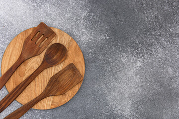Wooden kitchen utensils placed on a round wooden board on a gray textured surface