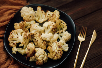 Delicious roasted cauliflower is arranged on a black plate showcasing its golden-brown texture