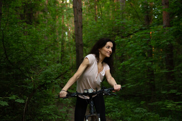 Beauty fun smiling sport woman biking on bicycle on path among green trees in a forest background....