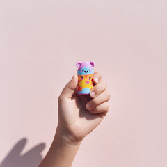 Childs hand holding a colorful, cartoonish toy against a soft pink backdrop. Ideal for illustrating concepts of childhood, play, creativity, and small wonders.