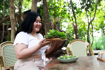 A cheerful plus-size woman holding a wooden tray filled with fresh green lettuce, symbolizing healthy eating and a balanced lifestyle