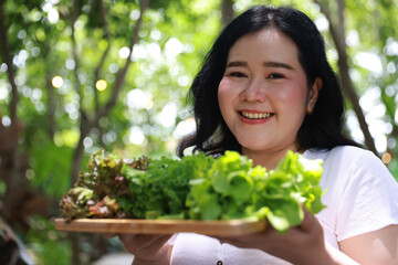 A smiling plus-size woman holding a wooden tray filled with fresh leafy greens,healthy living and natural food
