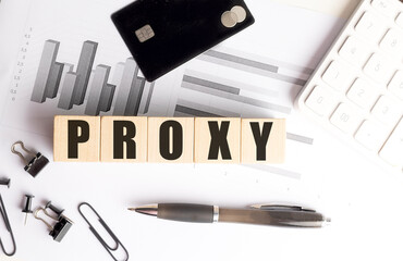 Proxy word on wooden blocks with charts, credit card, pen, clips and calculator on white office desk
