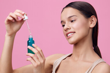 Young woman applying skincare serum from a dropper bottle, showcasing healthy skin and a joyful...