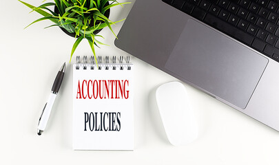 Accounting policies text written in notebook on white office desk with laptop, pen and potted plant