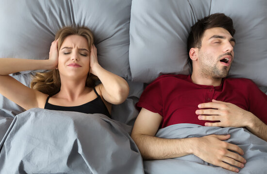 Snoring husband. Angry woman covering ears, top view in bed.