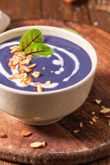 A bowl of creamy purple beet soup topped with a swirl of cream, toasted almonds, and fresh herbs.