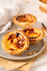 Three Pastel de Nata, Portuguese custard tarts, are presented on a plate with cinnamon and vanilla beans.