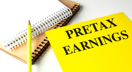 Pretax earnings text on yellow paper with spiral notebooks and pencil on white background