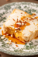 A close-up showcases a slice of traditional caramelized egg white pudding known as molotof or molotov, generously drizzled with sweet syrup and sprinkled with almond pieces, on a decorative plate