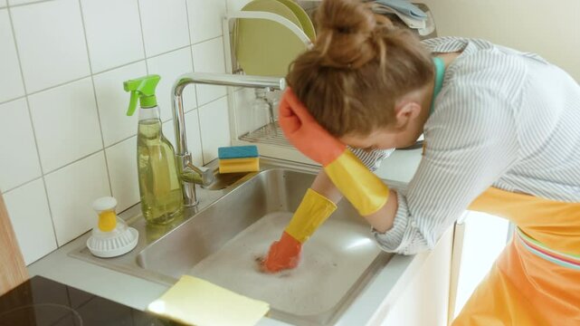 A tired person rests while facing a soapy sink, a plumbing issue. Fatigue and frustration with household chores are visible.