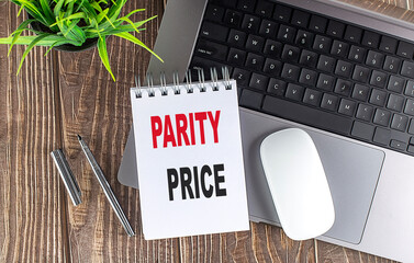 Parity price phrase on spiral notepad with laptop, mouse, pen and plant on wooden desktop
