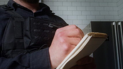 Closeup of a uniformed police officer writing in a notepad, possibly documenting a report or...