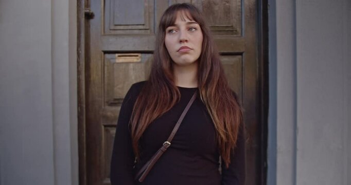 A young woman with long brown hair makes various facial expressions in front of a gray and brown door. Her reactions range from serious to contemplative.