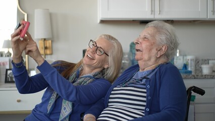 Fototapeta premium In a cozy indoor setting, a daughter shares joyful moments with her elderly mother as they connect through a smartphone, cherishing memories and love together.