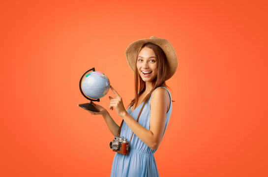 Active young woman with camera pointing at globe over yellow studio background, choosing destination to travel