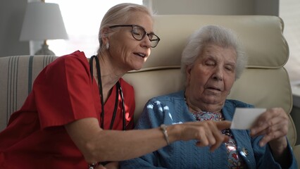 A caregiver interacts with an elderly woman in a healthcare facility, sharing memories and enhancing connection during their time together in a comfortable setting.